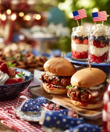 Festive Summer Picnic Table With 4th Of July Food Grilled Hot Dogs BBQ Chicken Burgers Fruit Skewers Flag Cake Berry Lemonade Checked Table Cloth